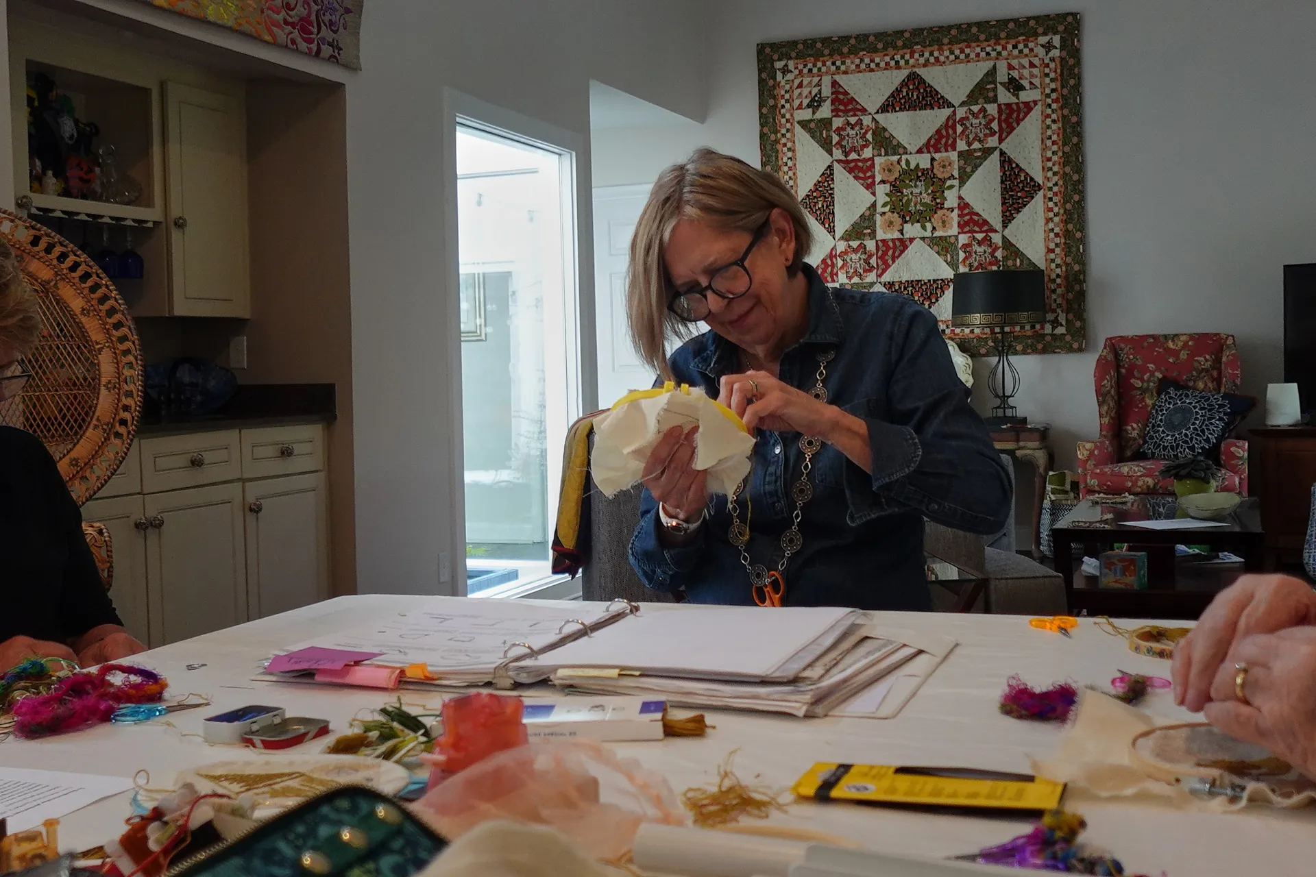 A volunteer stitcher embroidering a hooped panel at a table spread with coloured threads