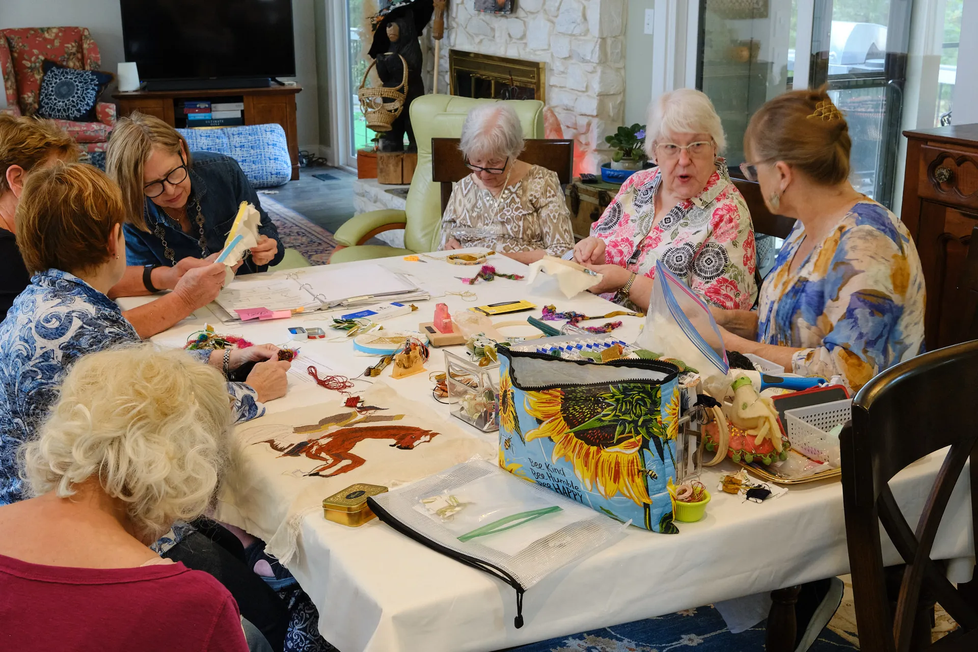 A circle of volunteer stitchers working together around a table, an embroidered fox taking shape on the linen