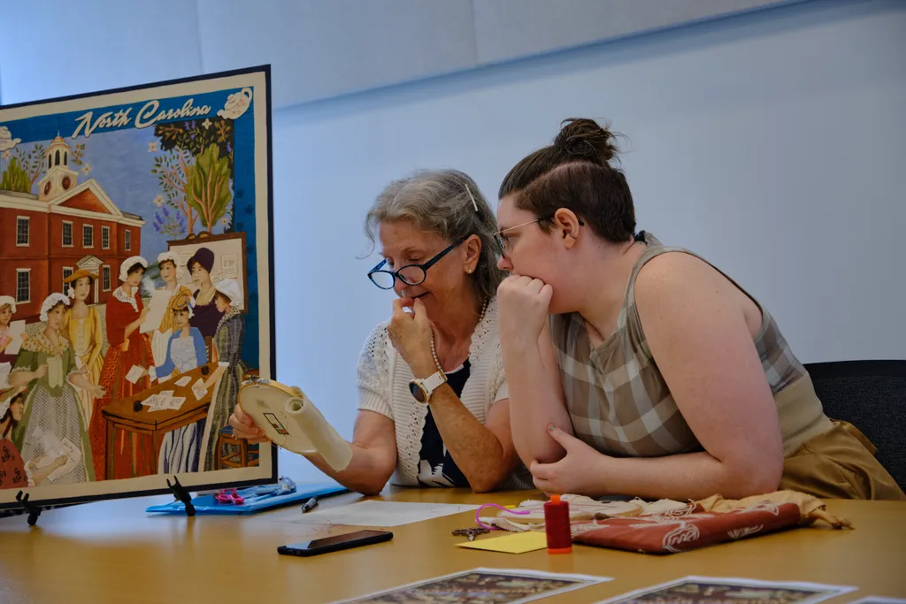 North Carolina Director Gail Smith and volunteer Corinne Burr examine a piece of embroidery at the Stitcher's Showcase