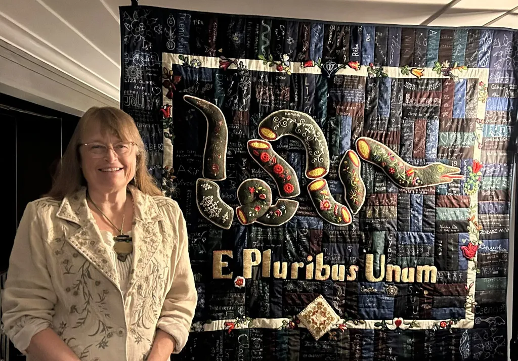 Karen Wallach smiling beside the finished panel, which hangs on the wall behind her